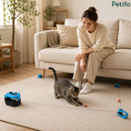 Woman sitting on a sofa watching her cat play with an automatic electronic interactive cat toy in the living room.